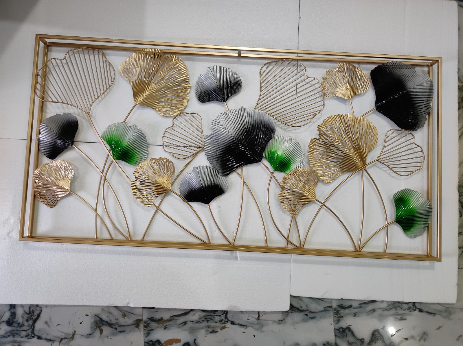 Decorative wall art with gold, black, and green leaves on a marble surface